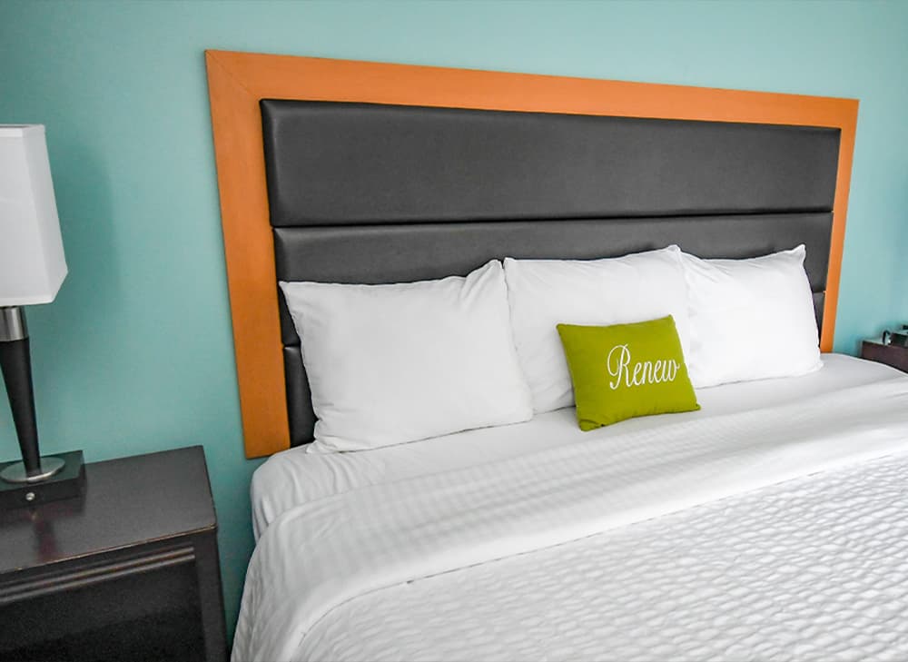 Inn at Saint Mary’s – Guest Room Bed with Accent Pillow Hotel bed with black leather headboard, white linens, green Renew accent pillow, and nightstand at Inn at Saint Mary's.