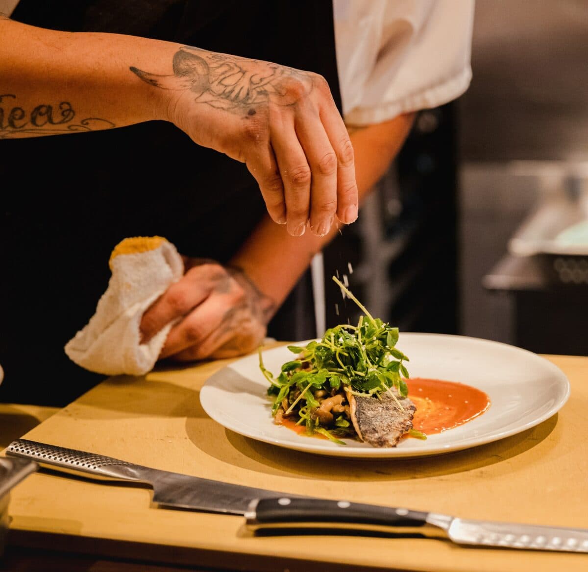 Chef Prepping Plate Chef sprinkling salt on plate of food with vegetables and sauce on it